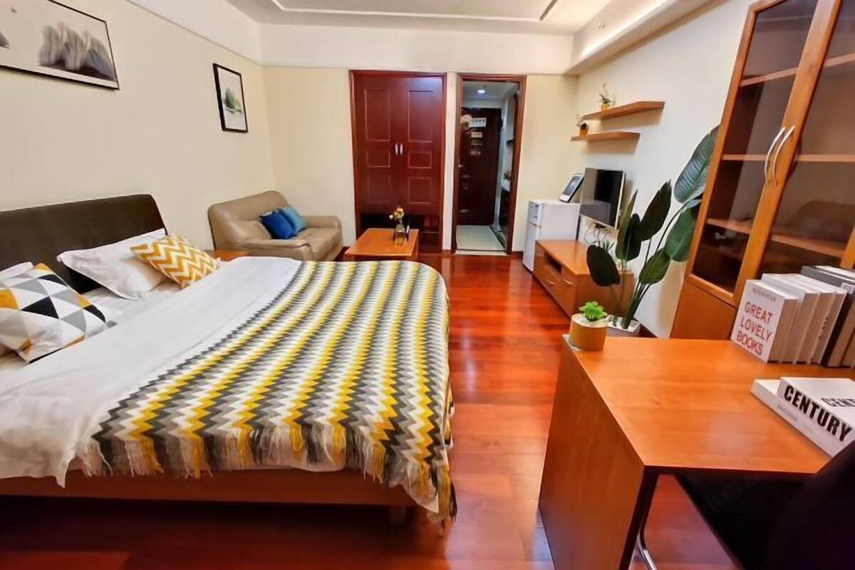 A hotel room with a bed, a sofa, a desk with books, and a TV.