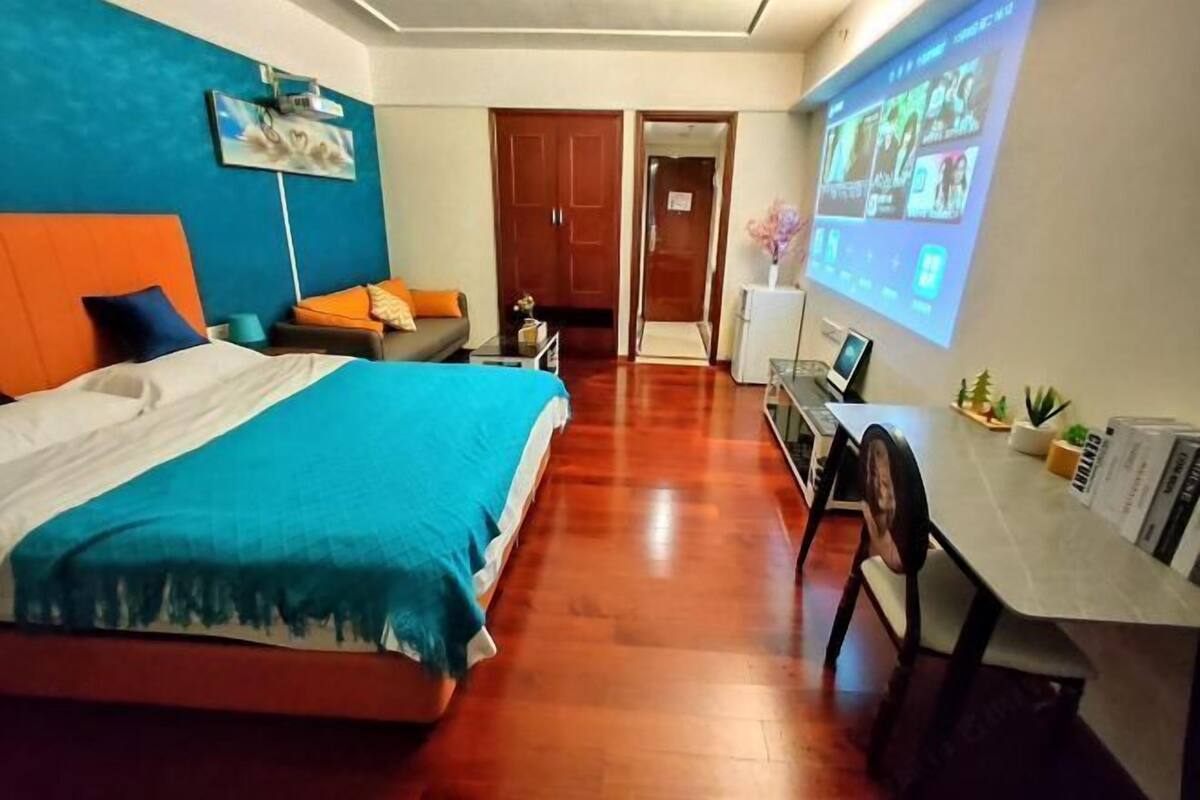 A hotel room with a bed, a desk, a chair, a TV screen, and a door.