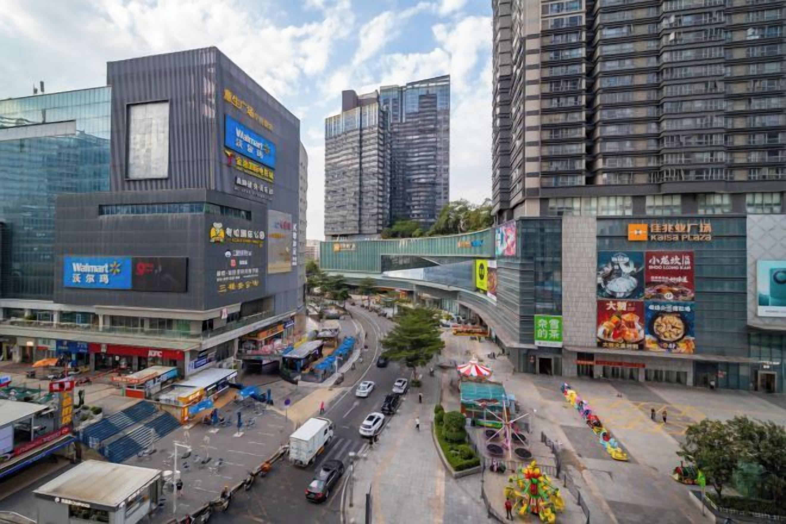 A busy urban street with modern buildings, a pedestrian bridge, and a Walmart store.