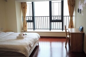 A hotel room with a bed, a desk, and a view of the outside through large windows. - Tianqin Mushang Hotel Apartment (Huizhou Kaisa Plaza) (Huizhou)