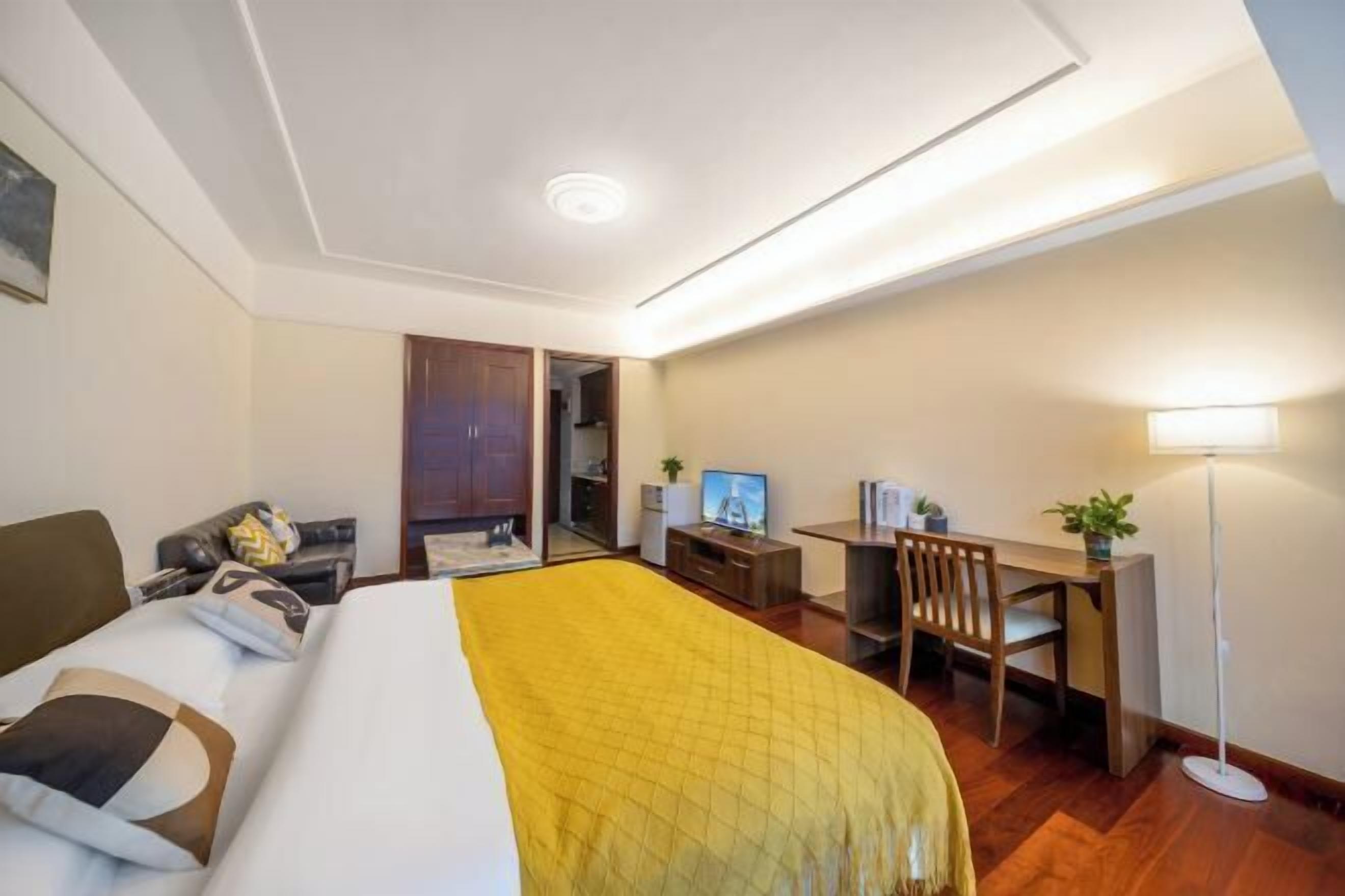 A hotel room with a bed, a desk, a chair, a TV, and a lamp.