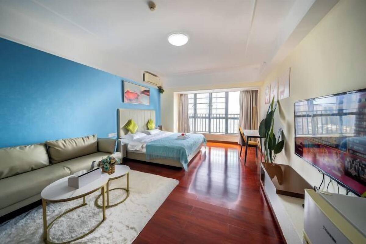 A modern hotel room with a bed, a sofa, a TV, and a large window.