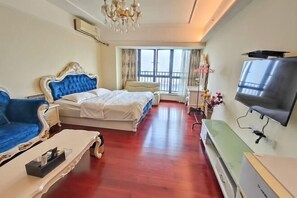 A hotel room with a large bed, a blue sofa, a television, and a balcony with curtains. - Tianqin Mushang Hotel Apartment (Huizhou Kaisa Plaza) (Huizhou)