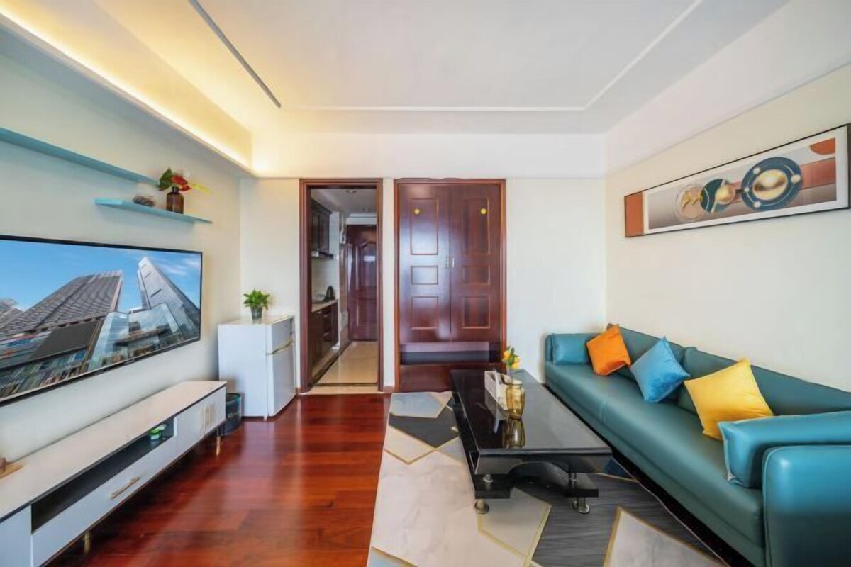 A modern living room with a flat-screen TV, a sofa with colorful cushions, a coffee table, and a wooden floor.