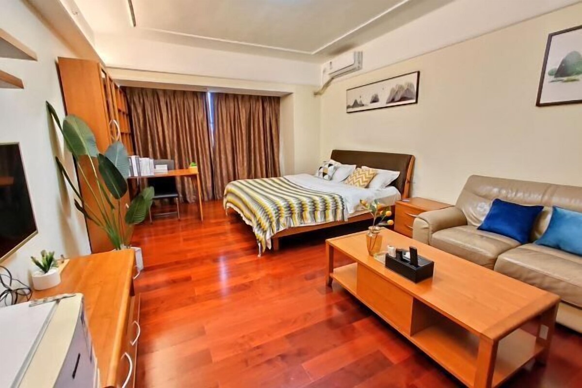 A hotel room with a bed, a sofa, a wooden coffee table, a TV, and a desk with a plant.
