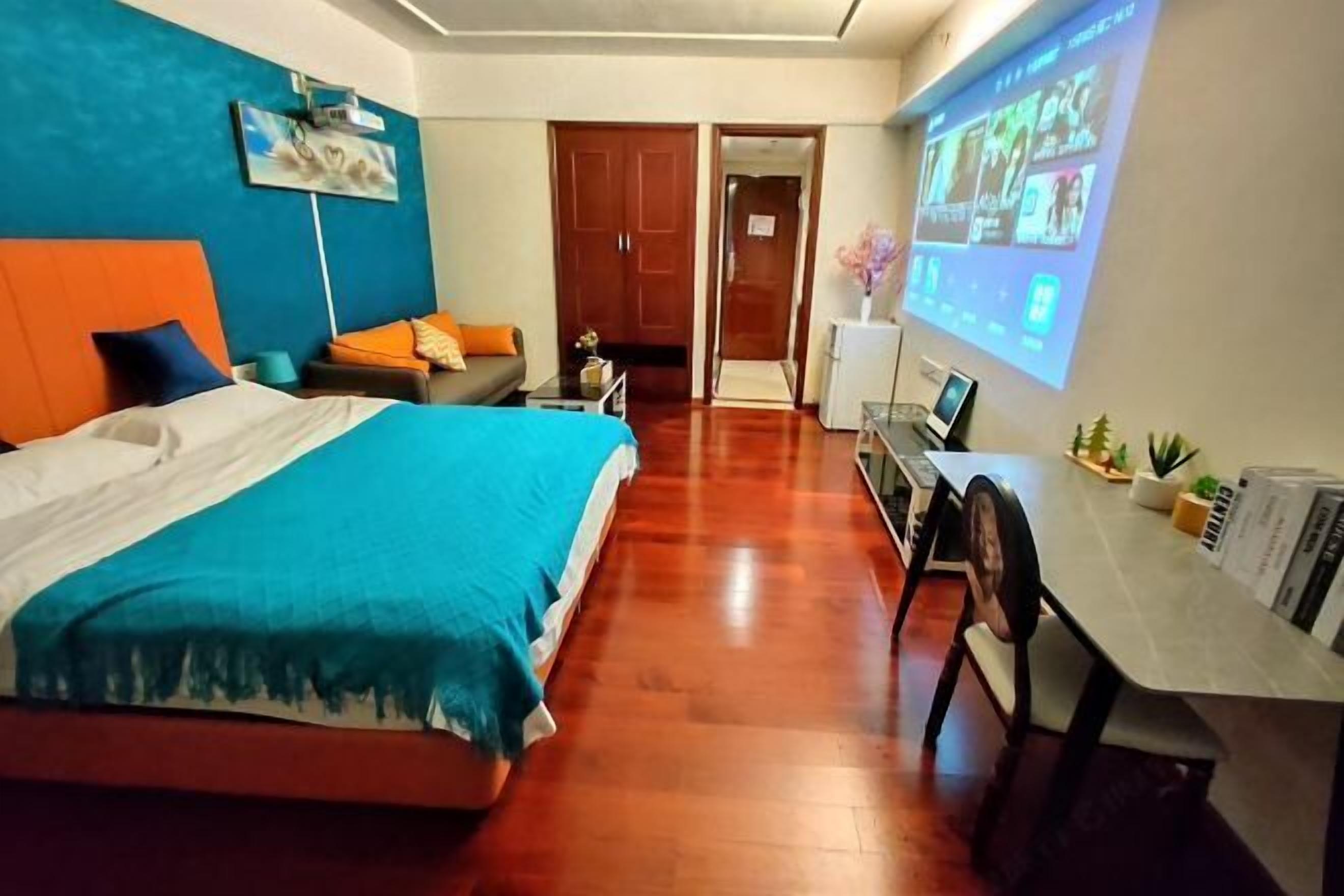 A hotel room with a bed, a desk, a chair, a TV screen, and a door.