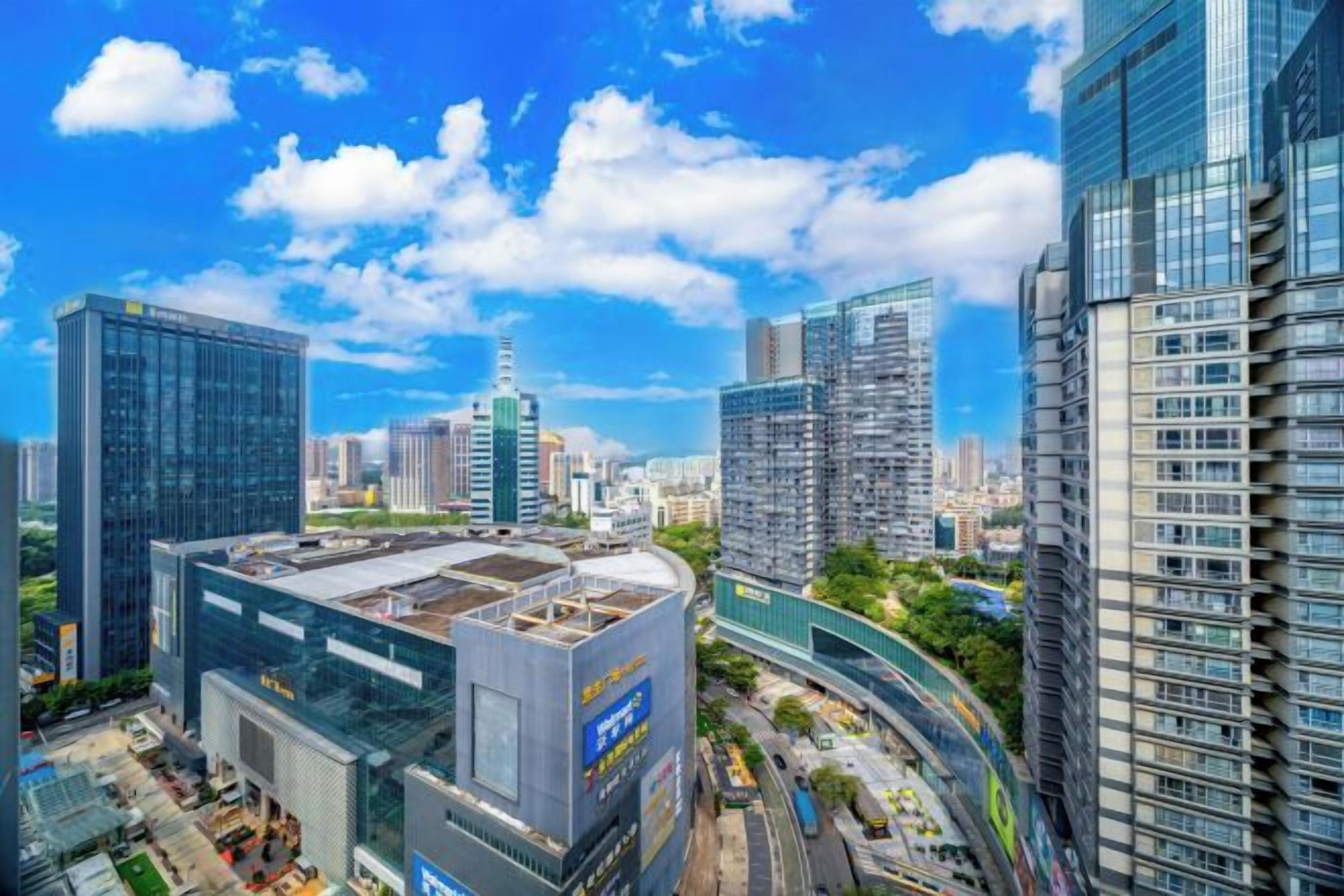 A cityscape with modern high-rise buildings, a clear sky, and a road with vehicles.
