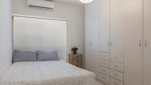 Une chambre à coucher comprenant un lit, une table de chevet, une commode et un appareil de climatisation.