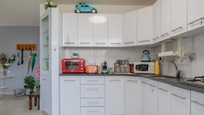 Une cuisine moderne avec des meubles blancs, un grille-pain rouge et orange, une bouilloire jaune et une petite voiture bleue posée sur le plan de travail.