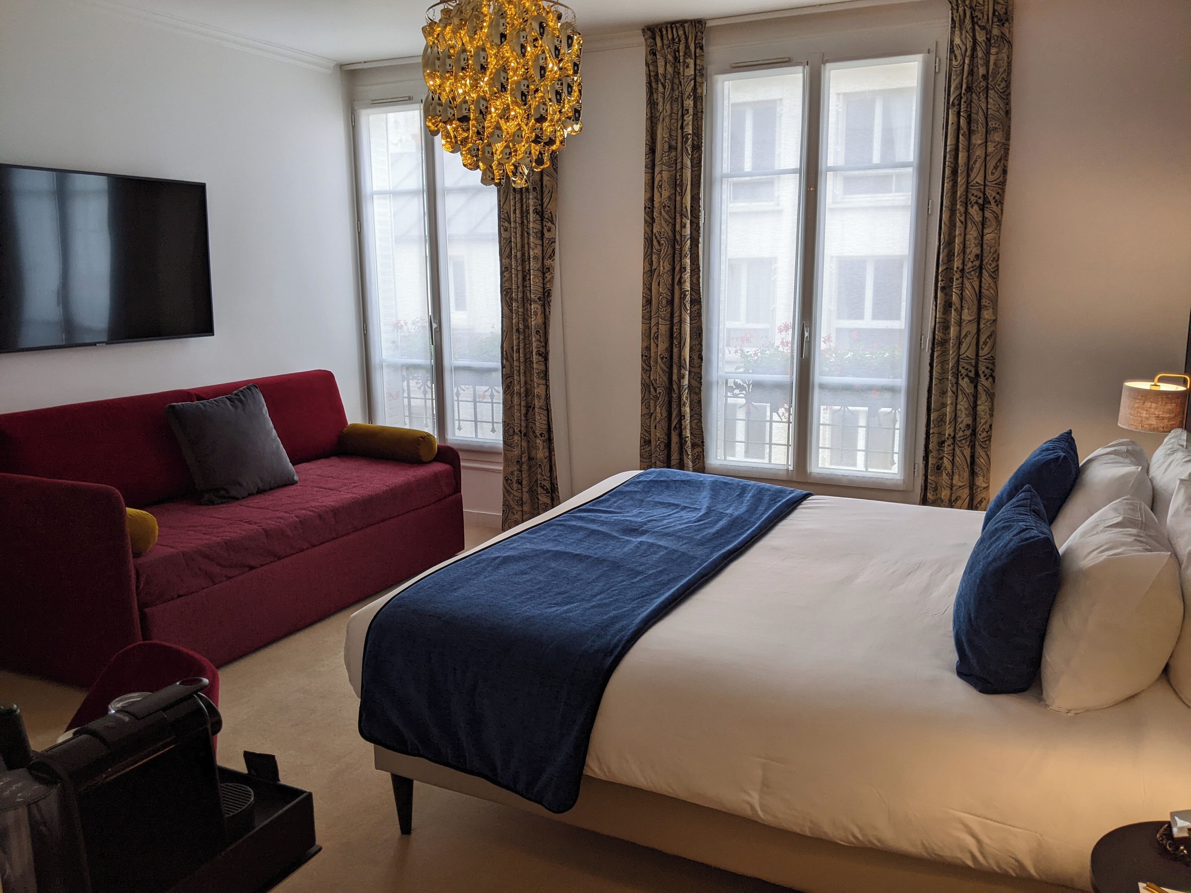 Una habitación de hotel con una cama grande, un sofá rojo, un televisor montado en la pared y una ventana con cortinas.