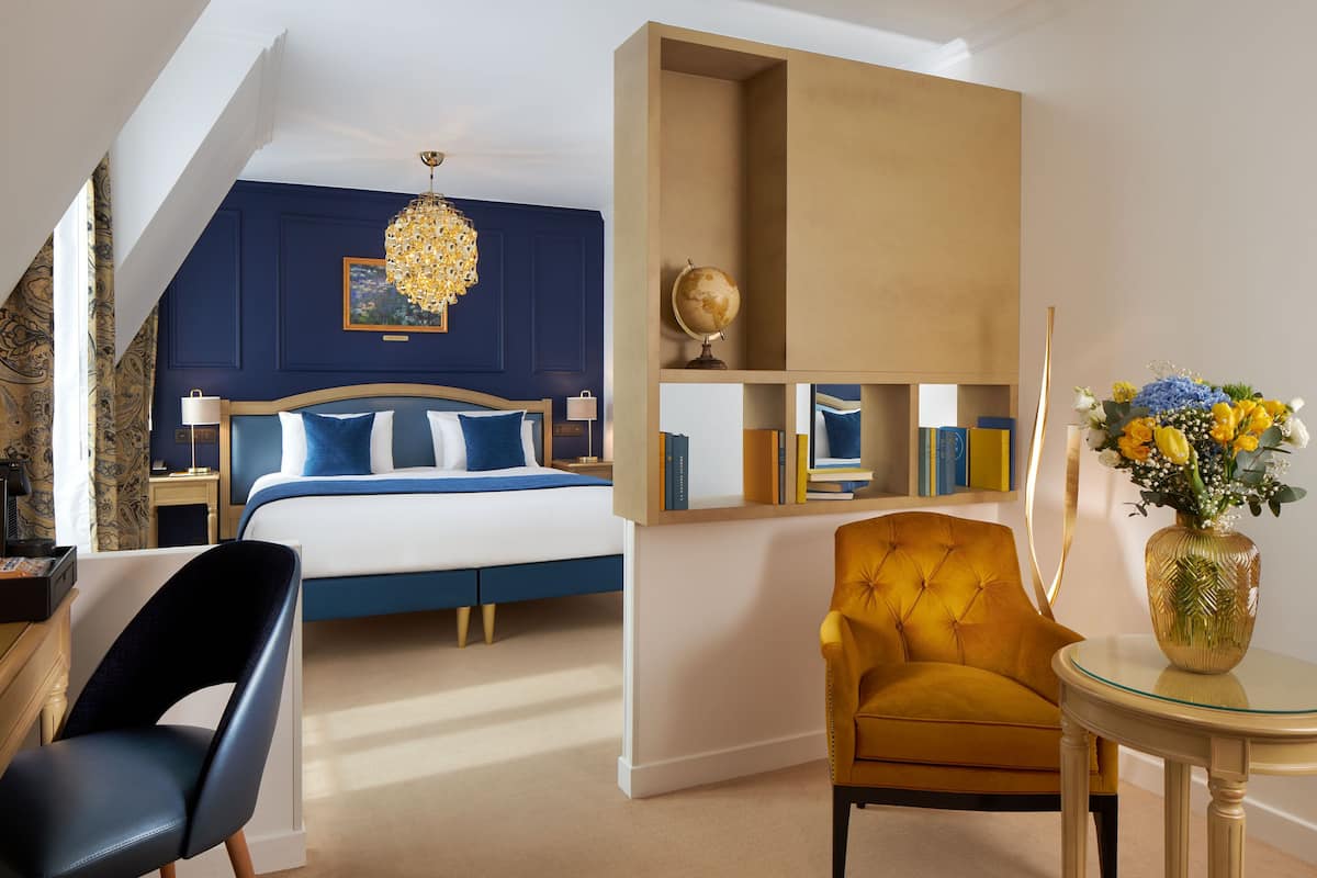 A bedroom with a bed, a chair, a table, and a bookshelf.
