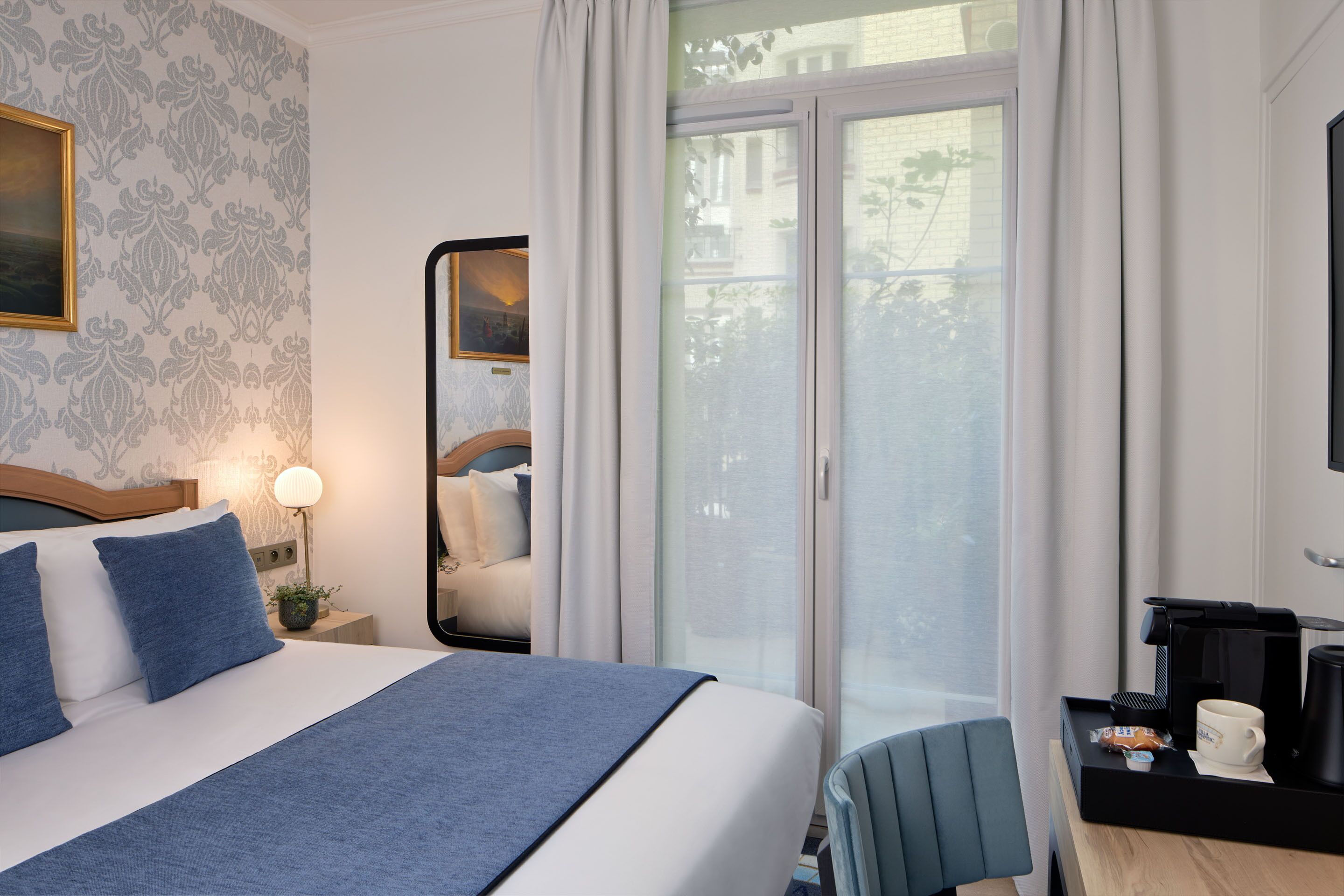 Une chambre d’hôtel avec un lit, une table de chevet, une lampe et une vue sur l’extérieur grâce à une porte vitrée.