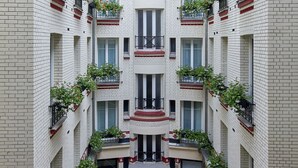 Un edificio de varios pisos con un patio central, balcones con plantas y un cielo despejado.