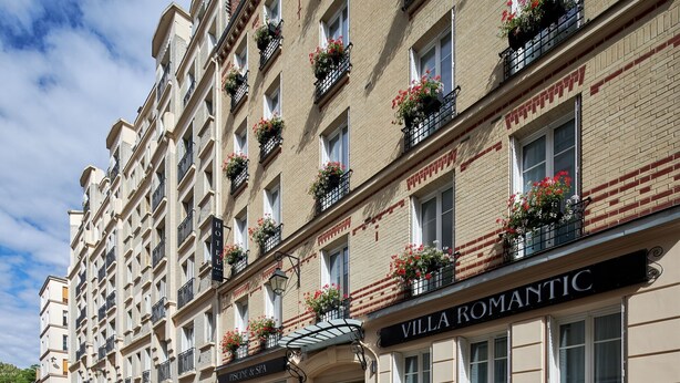 Un hotel de varios pisos con balcones decorados con flores, un spa visible y un restaurante llamado "Villa Romantic".
