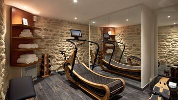 A room with stone walls, a treadmill, a massage table, and a TV.