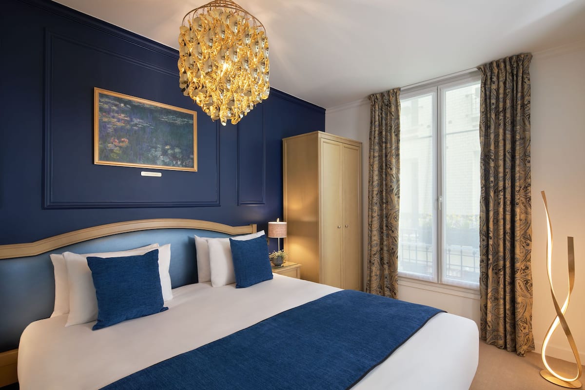 A bedroom with a large bed, a chandelier, a wardrobe, and a window with curtains.