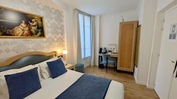 A hotel room with a bed, a desk, a chair, a lamp, and a painting on the wall.