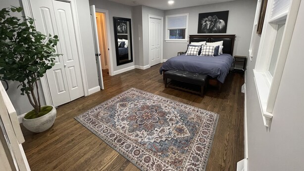 A bedroom with a bed, bedside tables, a nightstand, a bench, a potted plant, and a patterned rug.