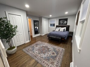 A bedroom with a bed, bedside tables, a nightstand, a bench, a potted plant, and a patterned rug.