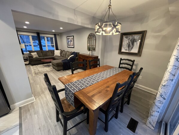 A dining area with a wooden table and chairs, a chandelier, and a view of a living room with a couch and a fireplace.
