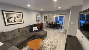 A modern living room with a sectional sofa, a coffee table, and a dining area with a wooden table and chairs.