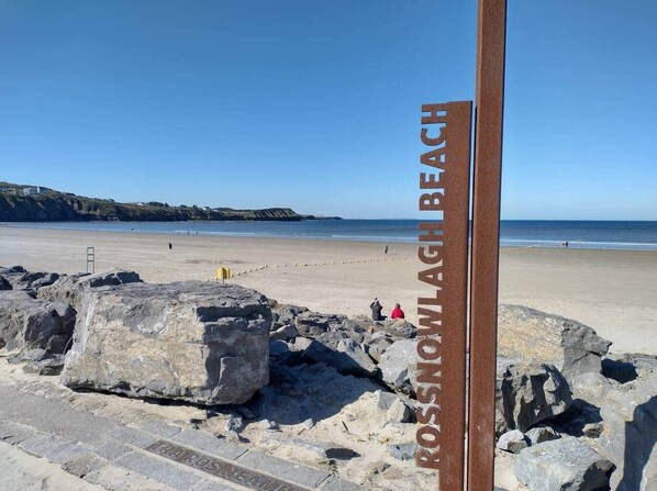 A beach with a sign reading 'ROSSONLAGH BEACH' and large rocks in the foreground.