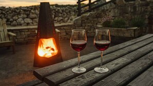 Two wine glasses on a wooden bench with a stone wall and a fire pit in the background. - The Rock, Creevy Cottages (Rossnowlagh)