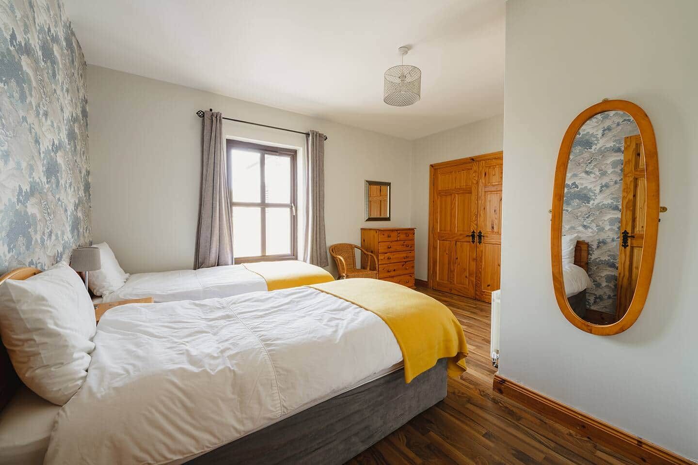 Ein Schlafzimmer mit zwei Betten, einem Schminktisch, einem Kleiderschrank, einem Spiegel und einem Fenster mit Vorhängen.