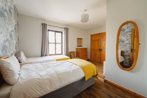 Ein Schlafzimmer mit zwei Betten, einem Schminktisch, einem Kleiderschrank, einem Spiegel und einem Fenster mit Vorhängen.