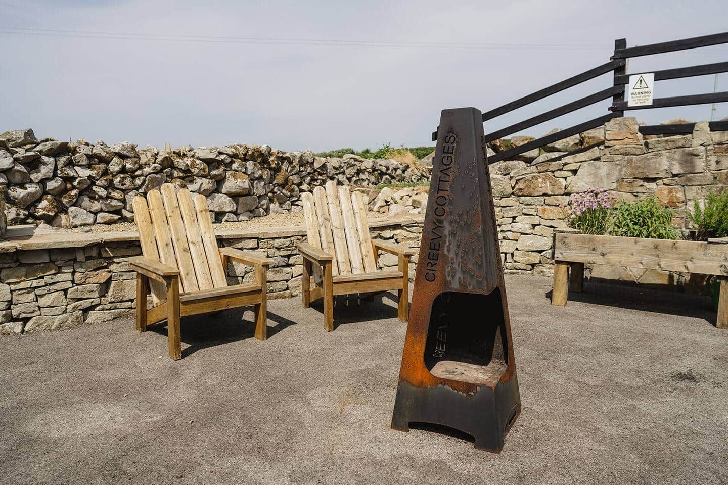 A stone wall, wooden chairs, and a metal sign with 'CREEVY COTTAGES' text.