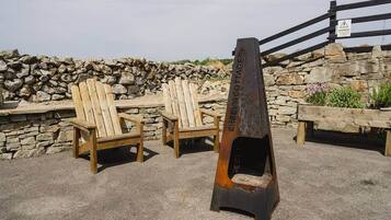 A stone wall, wooden chairs, and a metal sign with 'CREEVY COTTAGES' text.