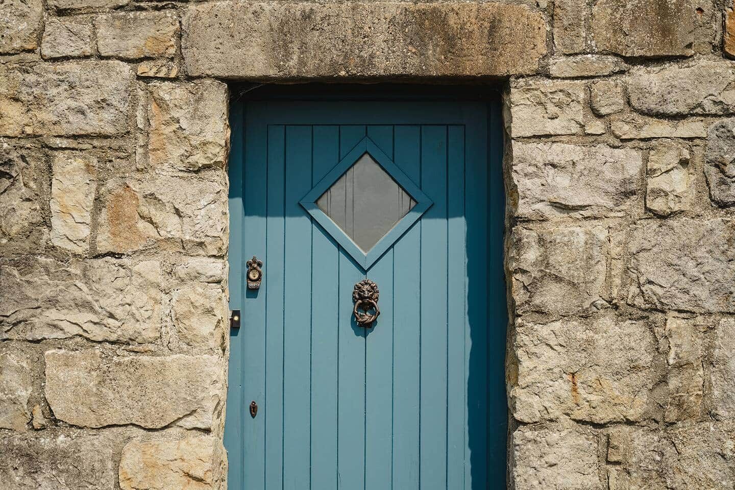 A stone wall with a blue door featuring a diamond-shaped window and two metal knockers.