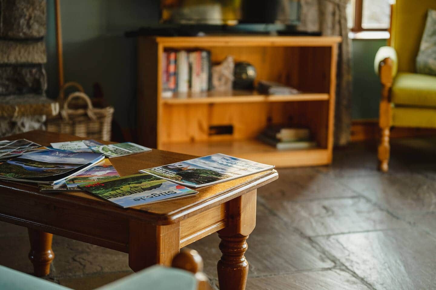 A wooden table with travel brochures, a bookshelf in the background, and a green chair.