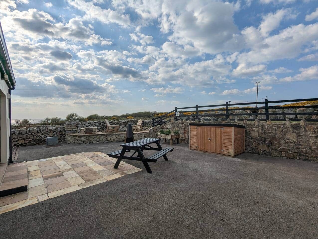 Ein Außenbereich mit einer Terrasse, einem Picknicktisch, einem Holzschrank und einer Steinmauer.
