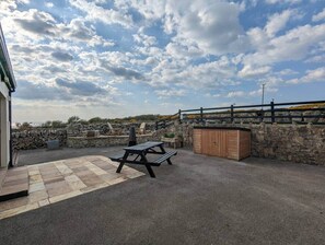 Ein Außenbereich mit einer Terrasse, einem Picknicktisch, einem Holzschrank und einer Steinmauer.