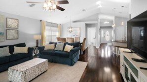 A spacious living room with a dark blue sofa set, a coffee table, and a ceiling fan. - 🐾Pet Friendly-Near Beach-4BR Shore Beats Work🐾 (Miramar Beach)