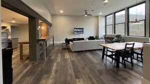 A modern kitchen with a large island, a dining area with a table and chairs, and a living area with a sofa and TV. - Riverside Loft with Huge Deck on GAP Trail (Confluence)