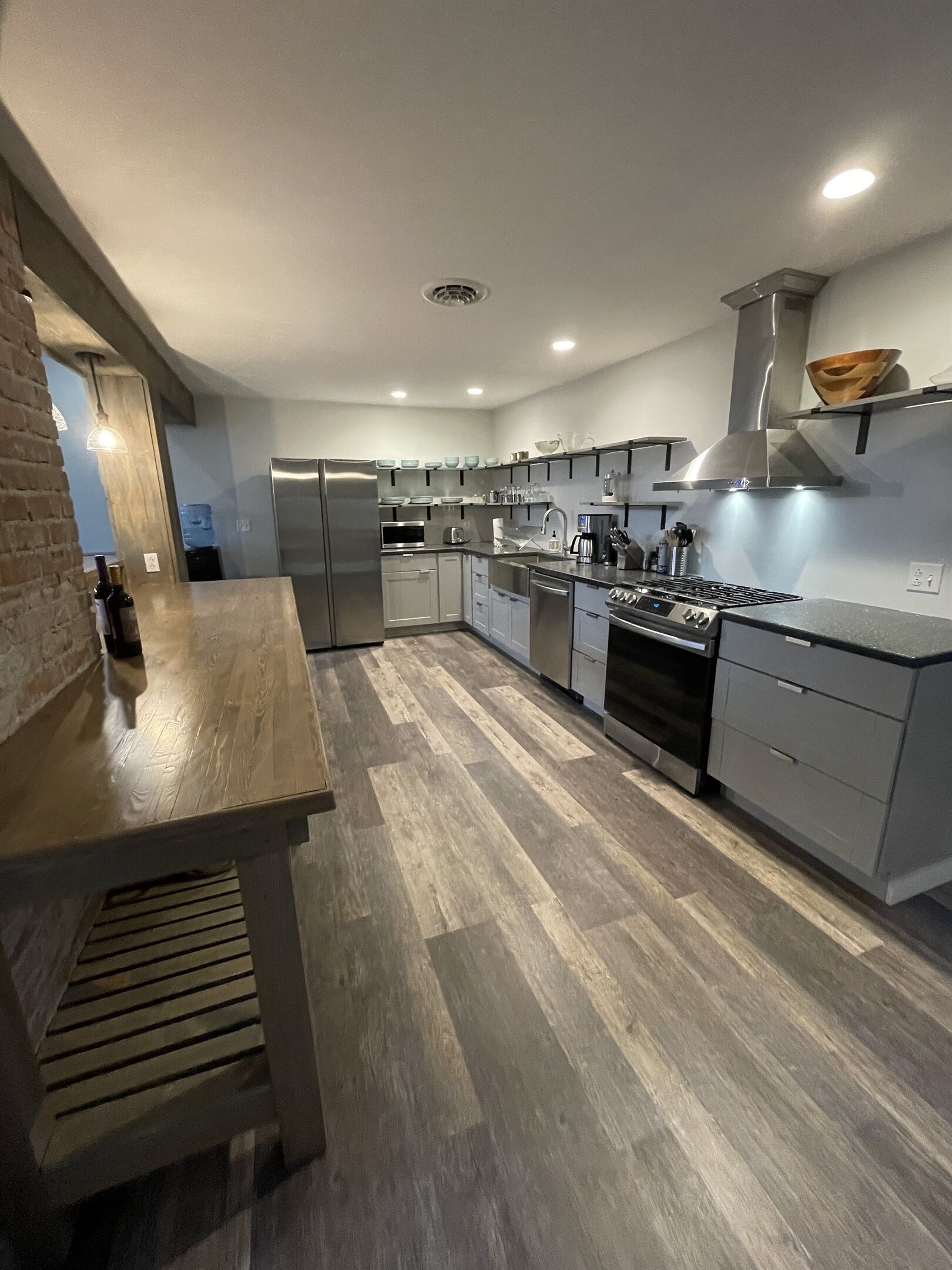 Una cocina moderna con electrodomésticos de acero inoxidable, piso de madera y una pared decorativa de ladrillo.
