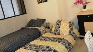 Une chambre avec deux lits, un bureau, une chaise, une fenêtre et un élément décoratif mural.