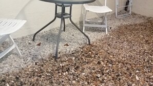 Un petit espace extérieur aménagé avec une table ronde et deux chaises blanches, le tout entouré de gravier.