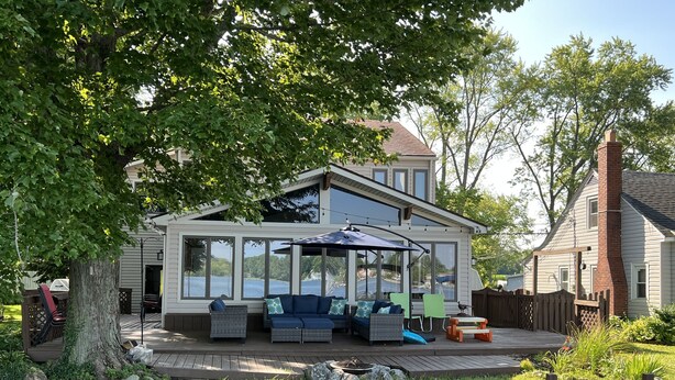 Ein Haus mit überdachter Terrasse, Sitzgelegenheiten im Freien und Blick aufs Wasser.