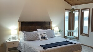 Ein Schlafzimmer mit einem großen Bett, einer Holzbalkendecke, einem Nachttisch mit Lampe und einem Fenster mit Vorhängen.
