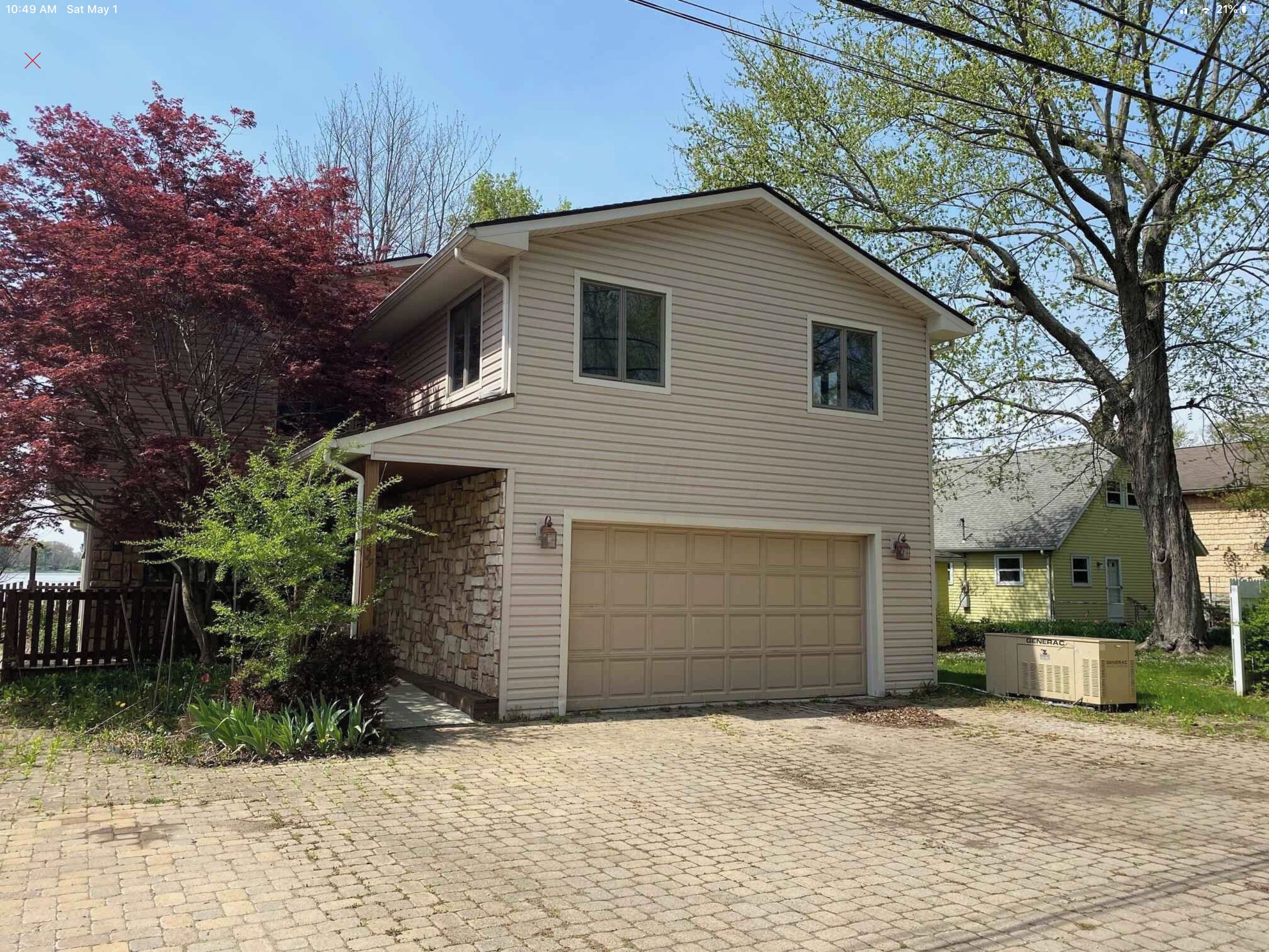 A two-story house with a garage, stone foundation, and a brick driveway.