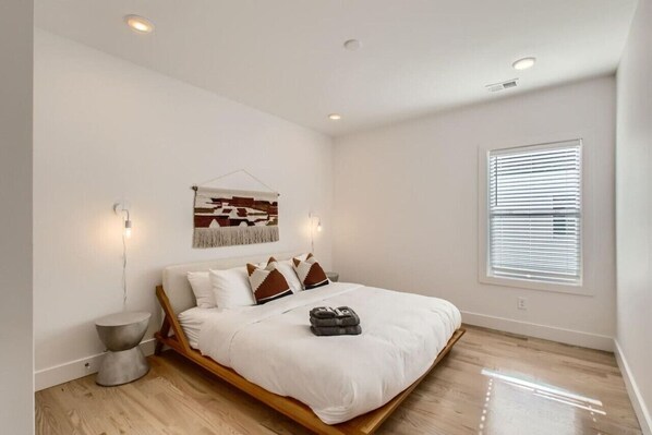A bedroom with a wooden bed frame, white bedding, a wall-mounted artwork, a bedside table, and a window with blinds. - 8 - Music Hill - The Music City Collection (Nashville)