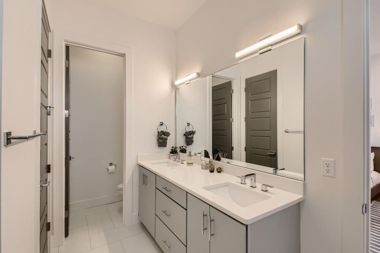 Un bagno moderno con un doppio lavandino, uno specchio grande e un water.