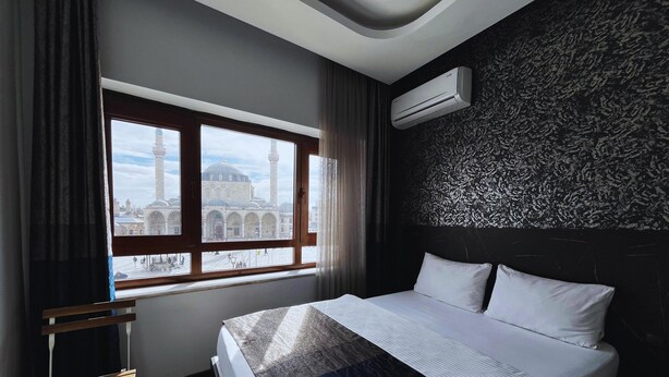 Habitación de hotel con una cama grande, una ventana con vistas a una mezquita y un equipo de aire acondicionado en la pared.