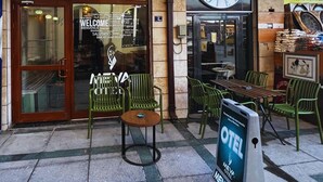 Exterior de un hotel con un letrero que dice "OTEL ÇINAR" y "MEVA HOTEL". Hay zonas de estar al aire libre con sillas y mesas verdes.