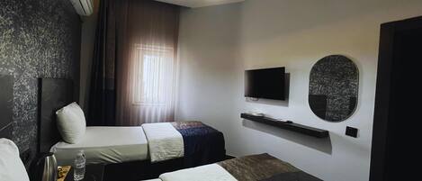 A hotel room with two beds, a flat-screen TV, a mirror, and a ceiling light.
