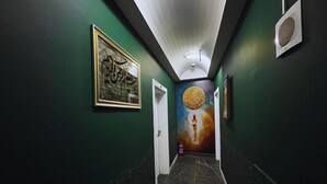 Un pasillo con paredes verdes, suelo de mármol, caligrafía enmarcadas y un mural de un cohete.