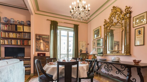 A room with a dining table, chairs, a chandelier, a bookshelf, and a television.